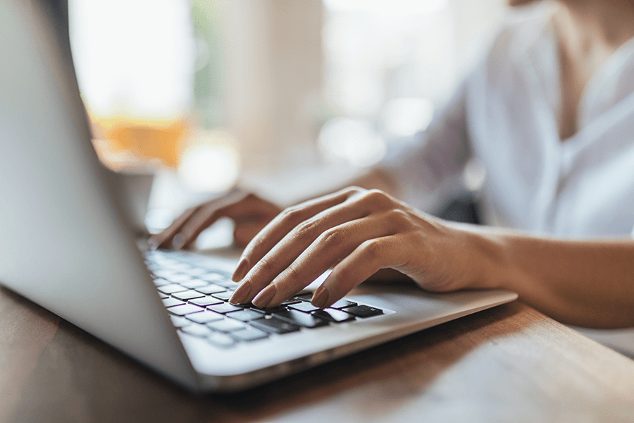 A close up of a woman's hands typing on a laptop inside of a cafe