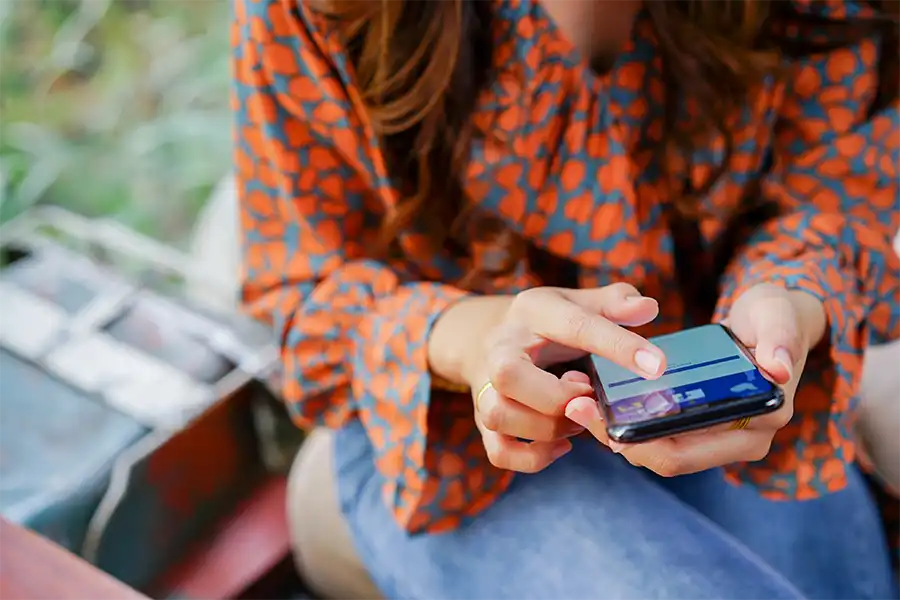 A woman sitting on a bench looking at Facebook on her Iphone.