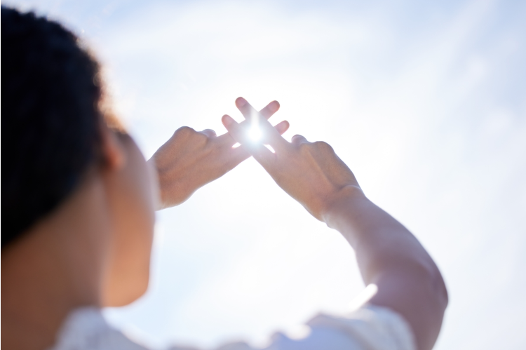 woman holding her hands up to the sun with her fingers intersected to create a hashtag with the sun shining through