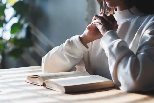 woman with clasped hands on a desktop with an open book on the counter