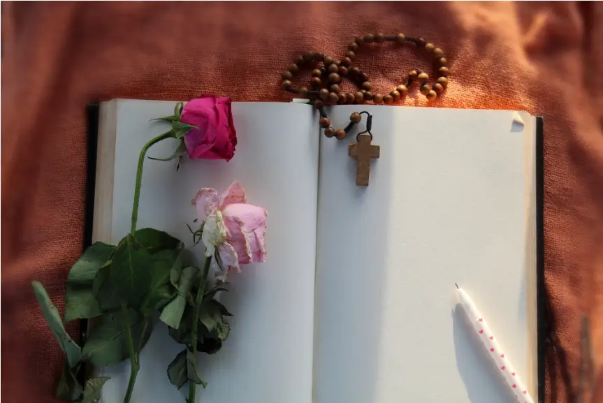 open book with blank white pages and a wooden rosary and two roses draped over the pages