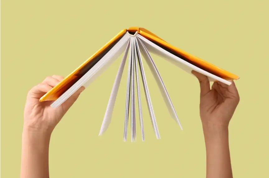 child’s hands holding up an open book against a yellow background