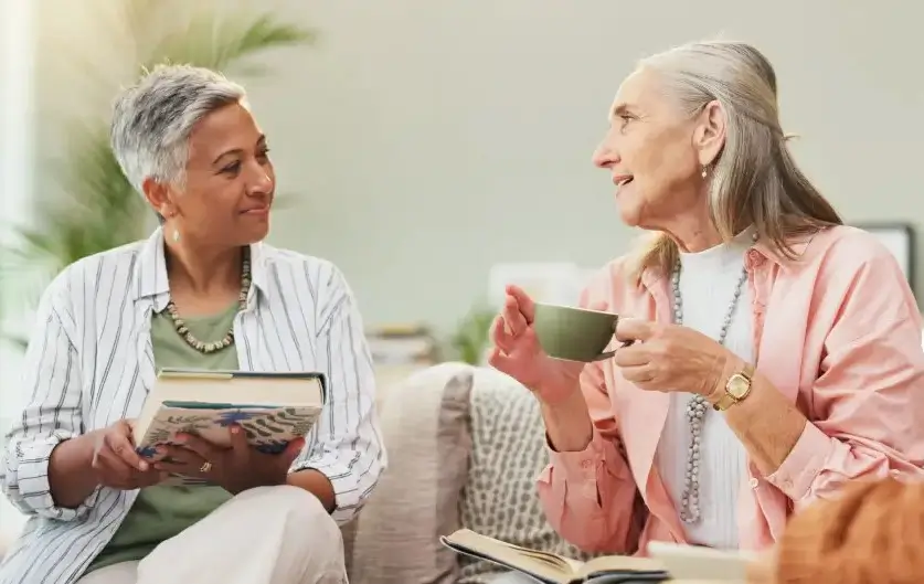 middle-aged woman reading her friend’s in-progress book over tea