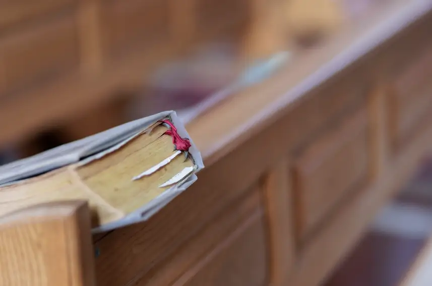 close-up of a light gray bound book leaning on the shelf of a church pew